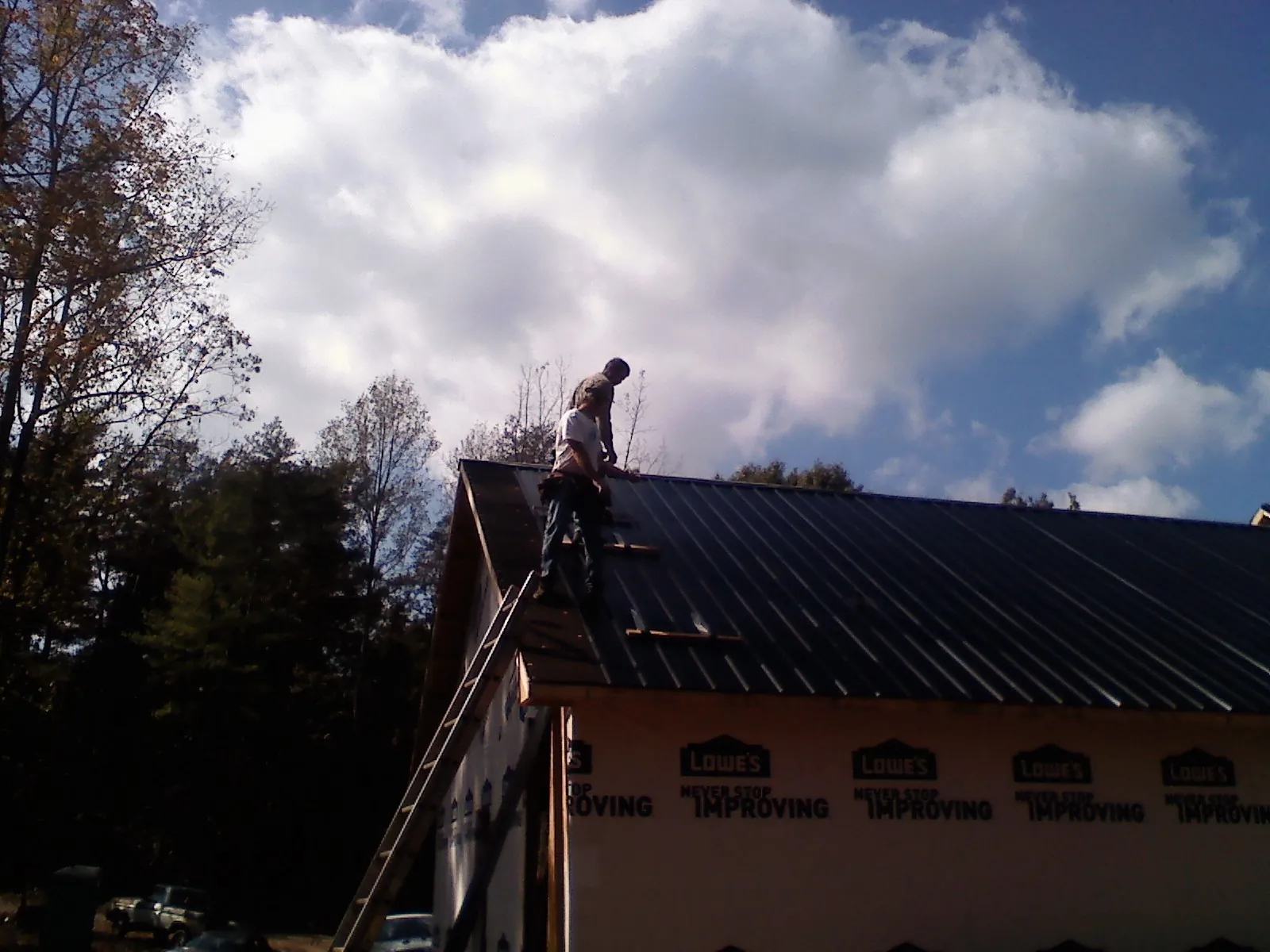 Roofer fastening dark metal panels high against a cloudy sky, from a Roof Inspection job in Lebanon